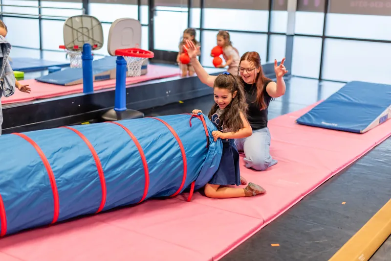 Girl crawling out of a play tunnel while her teacher cheers