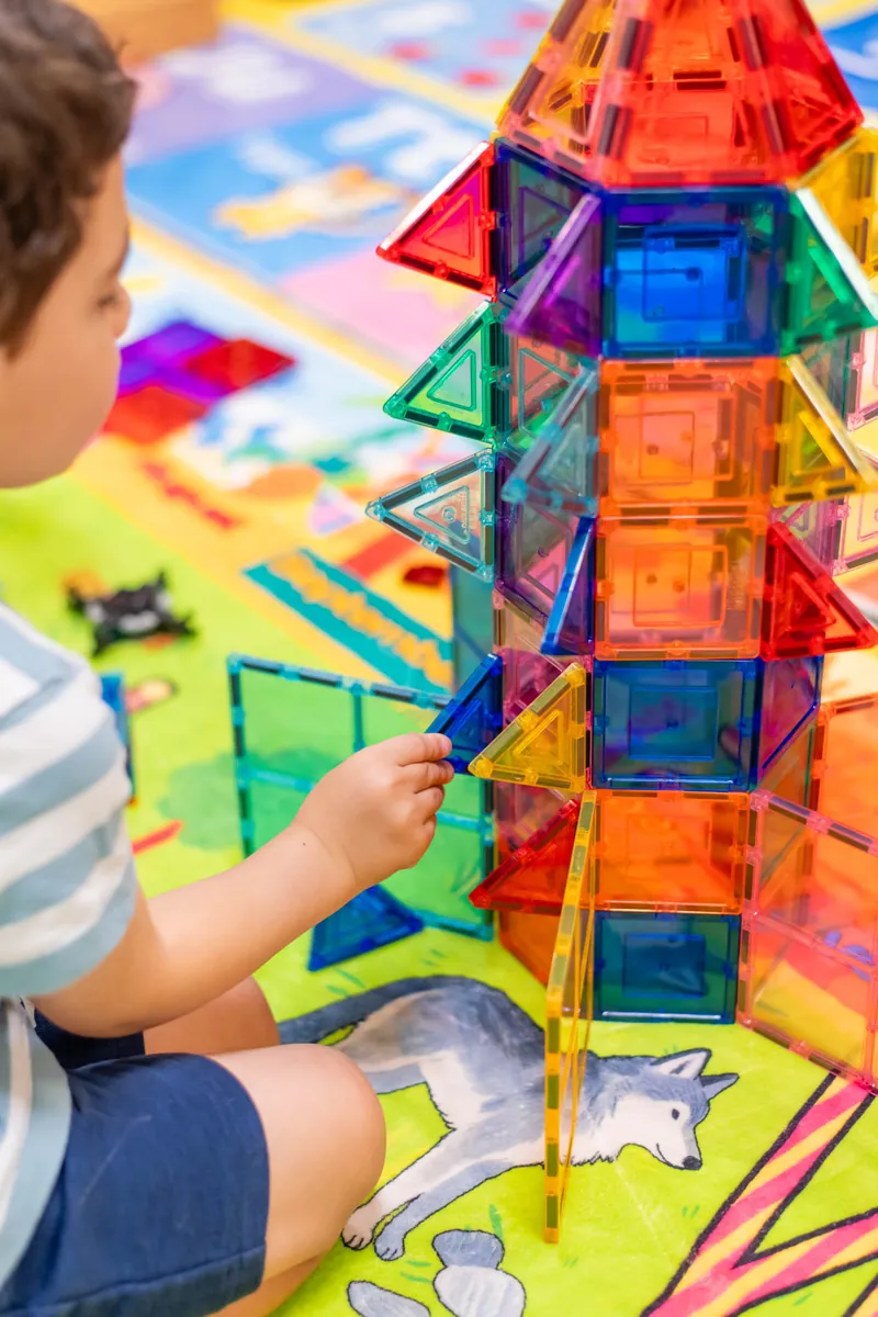 Child building a tall tower out of colorful magnetic tiles