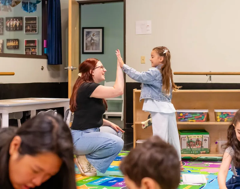 Teacher giving a preschooler a high five in the classroom