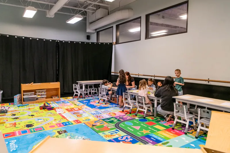 Bright preschool classroom with small tables and a colorful play rug