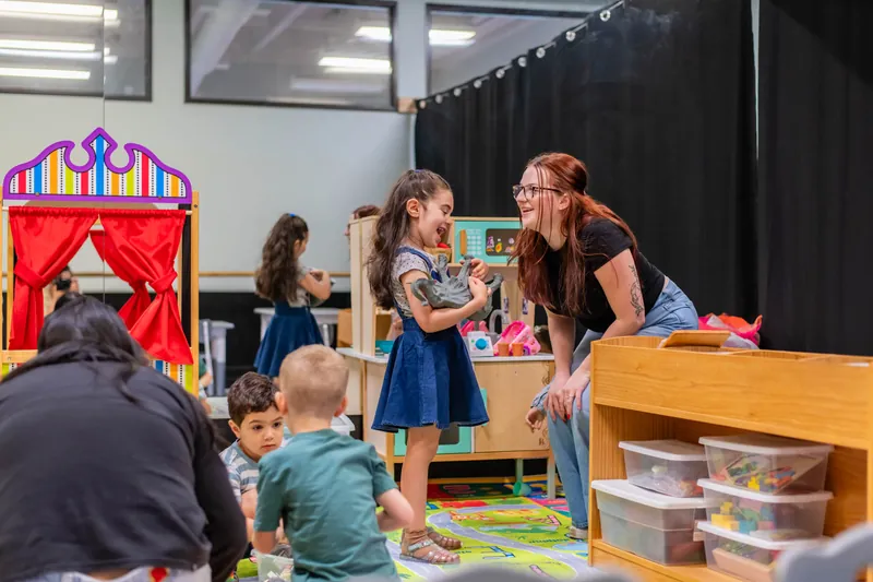 Girl showing her teacher a toy next to the puppet theater
