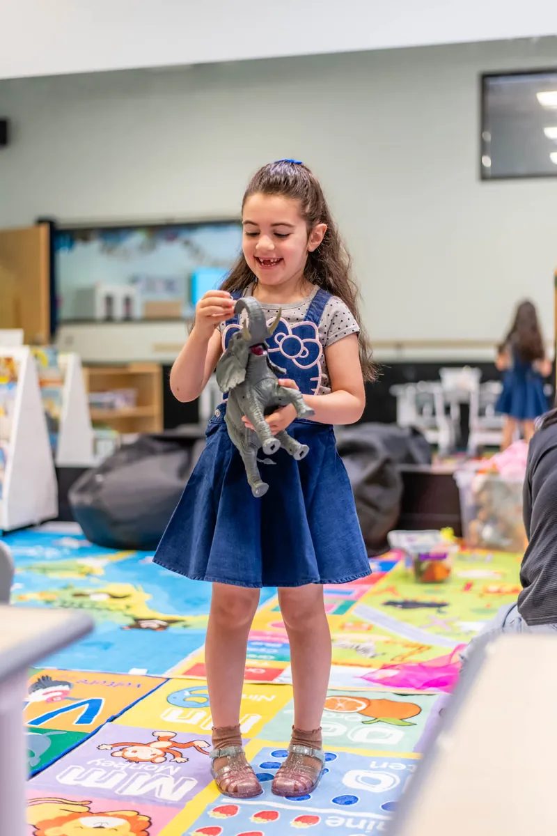 Smiling preschool girl holding a toy in the child care classroom