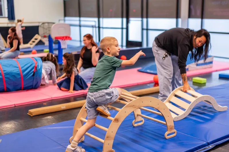 Boy climbing a wooden arch in the movement room with a teacher spotting